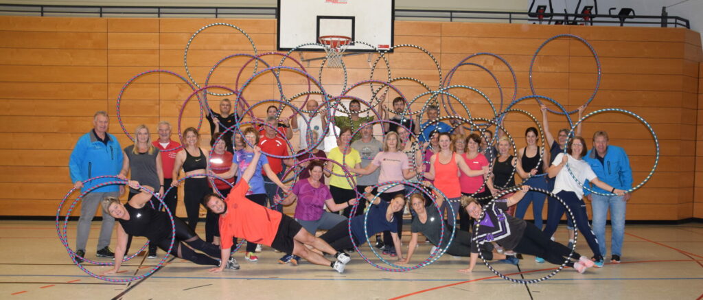 Ein Gruppenbild von einer großen Gruppe Menschen in einer Sporthalle. Sie posieren mit Hula-Hoop-Reifen.