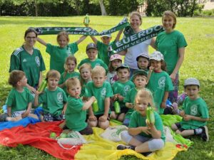 Kinder und Trainerinnen der Turnabteilung des TSV Euerdorf halten auf dem Rasen sitzend Vereinsschals in die Höhe.