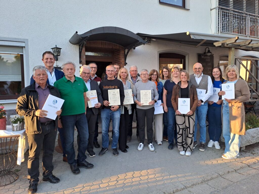 Mehrere Personen lächeln für ein Foto vor einem Gebäude in die Kamera. Sie halten Urkunden in der Hand.