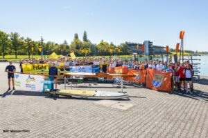 Menschen stehen vor der Regattaanlage München und halten Banner und Paddel in die Höhe
