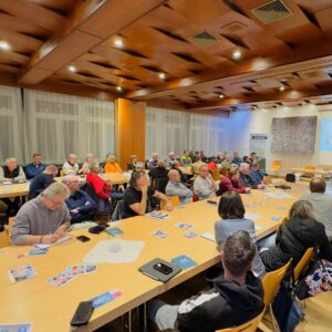 Mehrere Menschen sitzen in einem Raum und schenken der vortragenden Person ihre Aufmerksamkeit