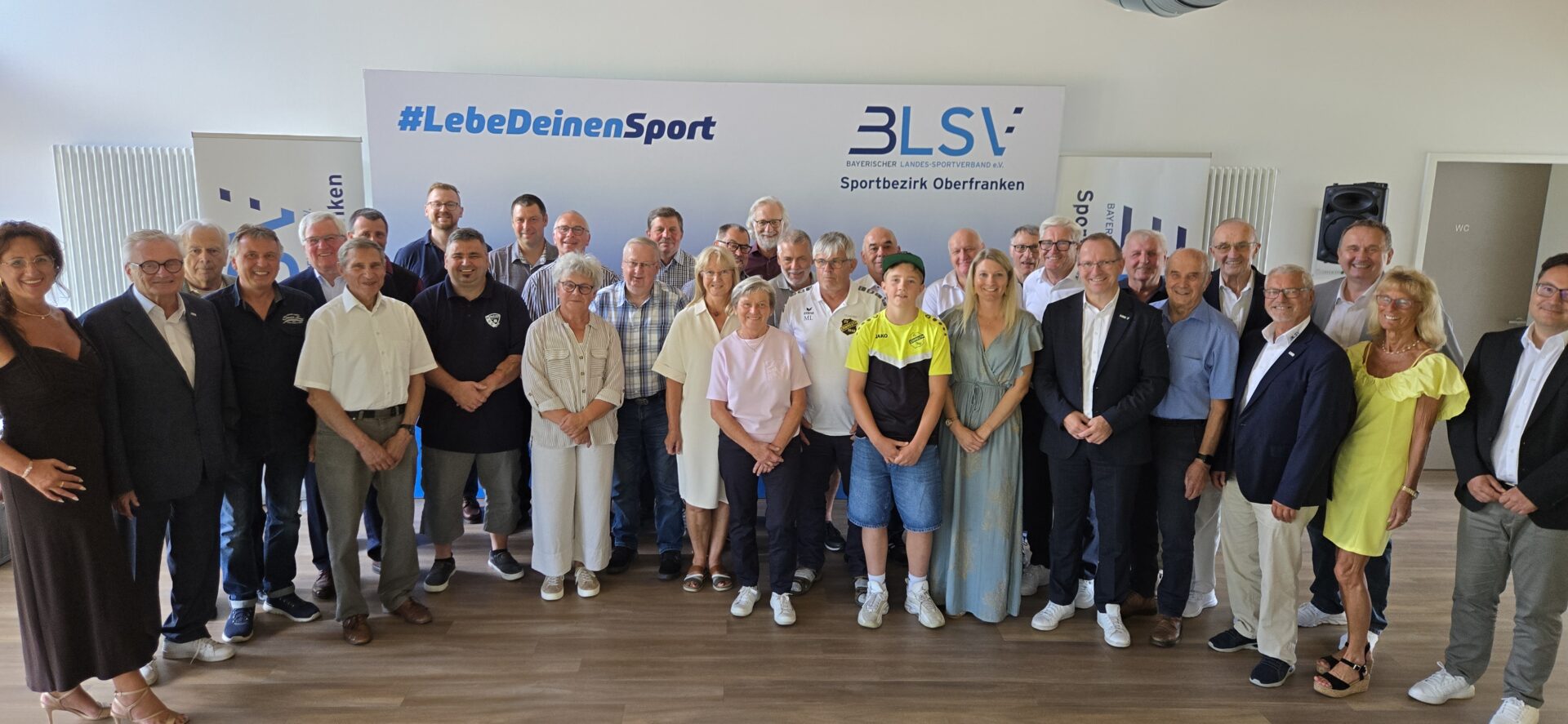Menschen sitzen auf einer Bank und lächeln für ein Gruppenbild in die Kamera.